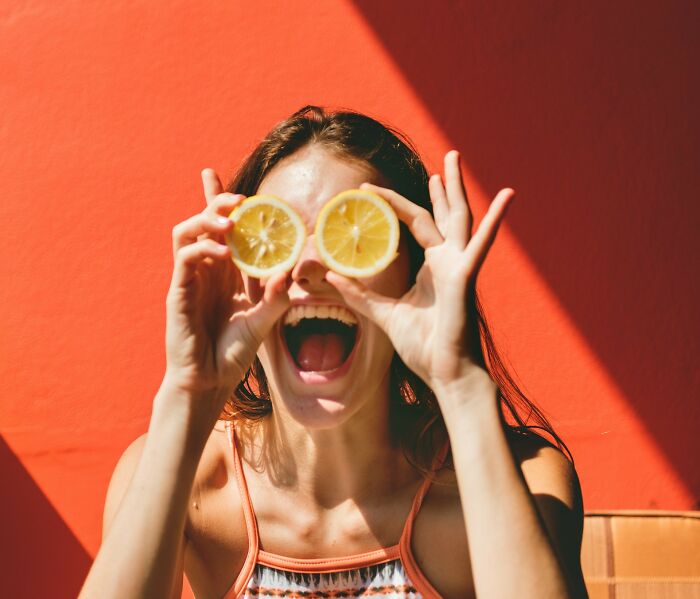 A joyful woman holding lemon slices over her eyes, illustrating women's health and gynecologist advice.