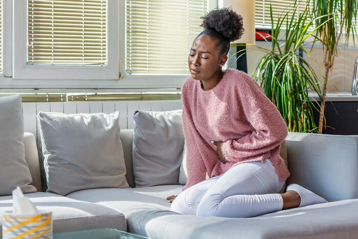 A woman on a couch experiencing abdominal pain, seeking gynecologist advice for women's health.