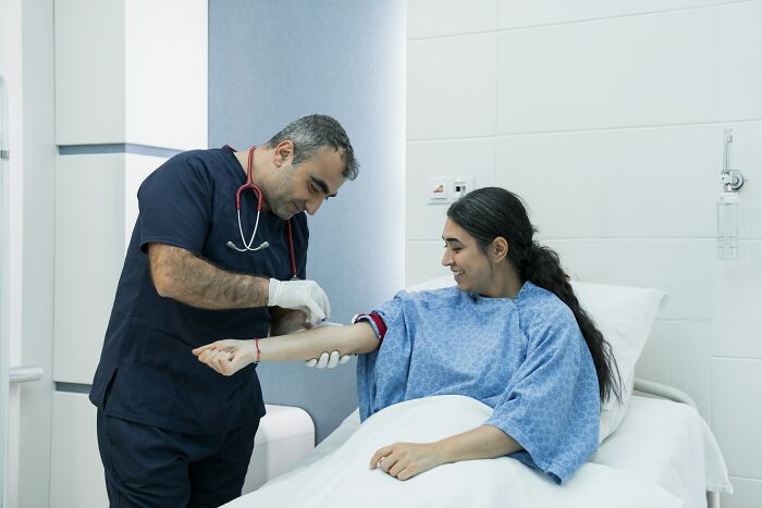 A doctor draws blood from a smiling woman in a hospital bed, showing the care women receive from gynecologists.