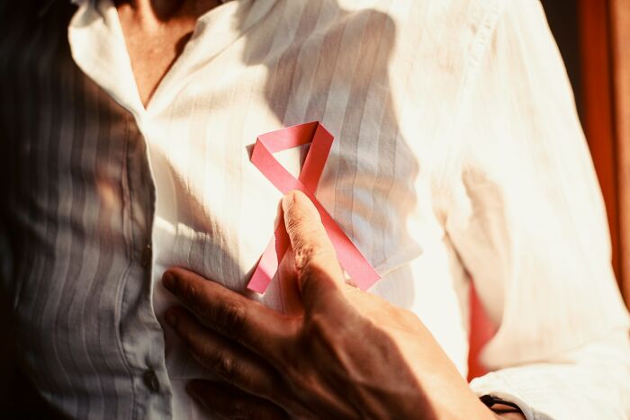 A woman's hand holds a pink ribbon on her chest, symbolizing awareness and advice from gynecologists.