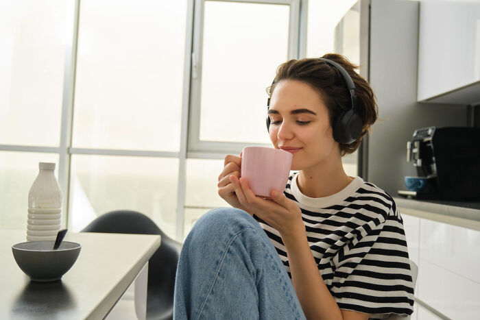 A woman enjoying a hot drink and music, finding comfort from gynecologists advice.