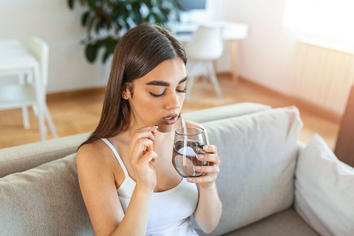 Woman taking a pill with water on a couch, highlighting health advice from gynecologists for women.