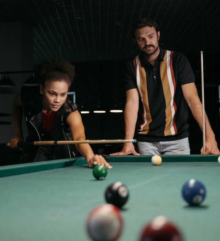A woman plays pool on a first date while a man watches, potentially revealing first date red flags.
