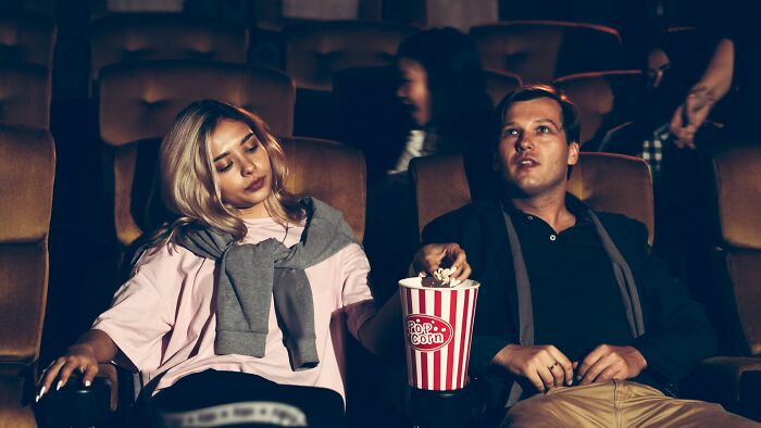 A woman sleeping in a movie theater next to an alert man eating popcorn, a first date red flag for boredom.