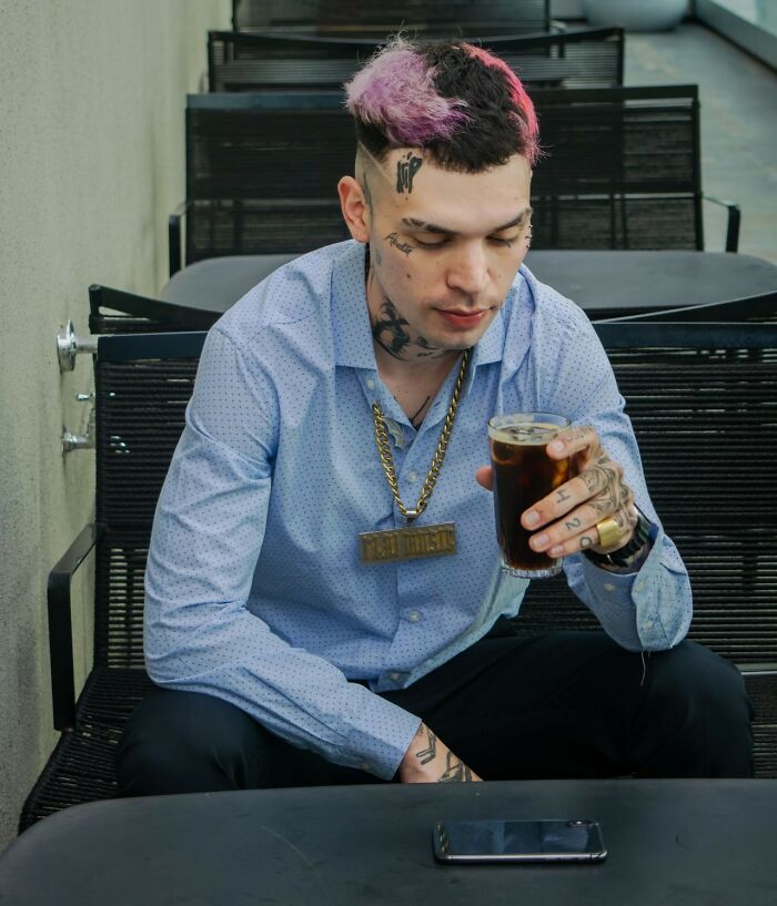 Man with tattoos and pink hair holding a drink, a potential first date red flag if judgment is involved.