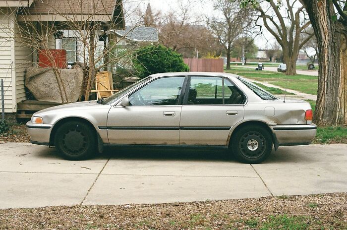 Old car with a dented bumper parked on a driveway, potentially a first date red flag for high expectations.