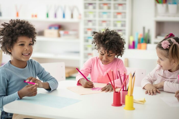 Three young children drawing and coloring at a table in a bright classroom, unrelated to first date red flags.