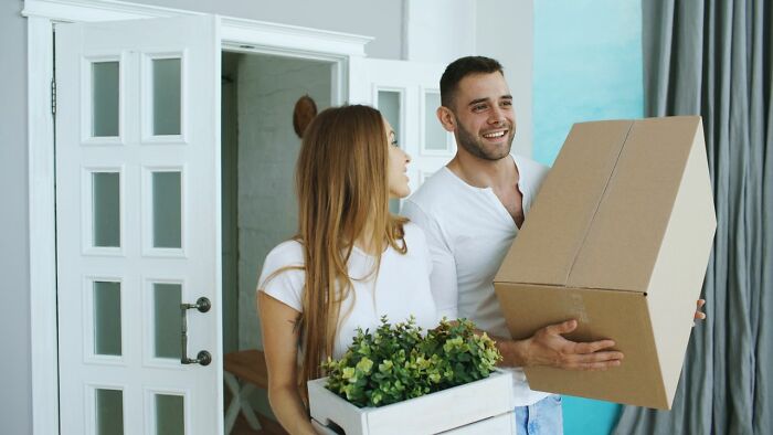 A smiling couple carries boxes and a plant, suggesting a successful relationship beyond first date red flags.
