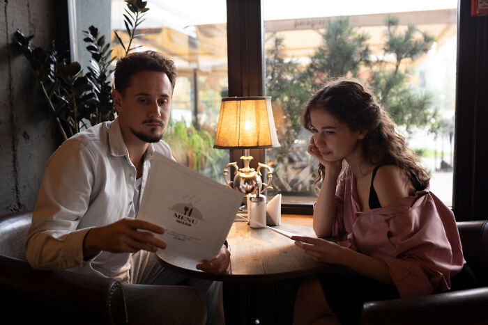 A couple looks at menus in a restaurant, potentially on a first date, observing for any red flags.