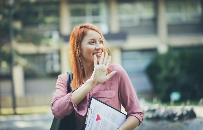 A happy woman with red hair waves, a positive sign on a first date or avoiding red flags.