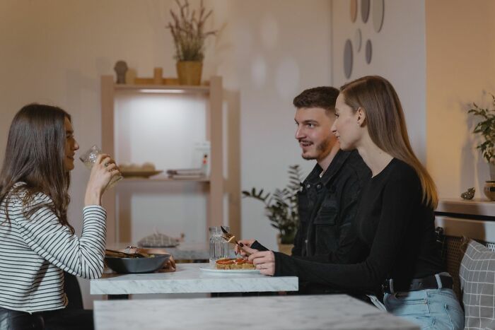 Three people sit at a table in a restaurant, a couple on a first date and a friend with a drink.