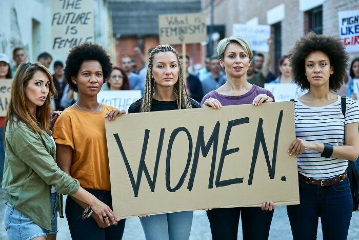 A group of women holding a sign that says WOMEN. Many women experience shocking first date red flags.