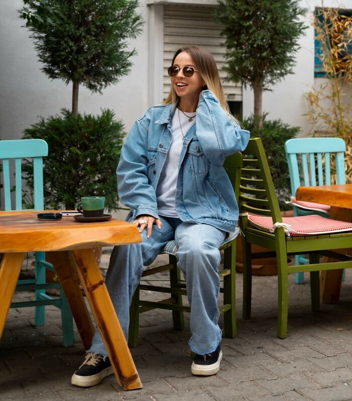 Smiling woman in denim jacket at an outdoor cafe, a possible first date red flag if she is easily bored.
