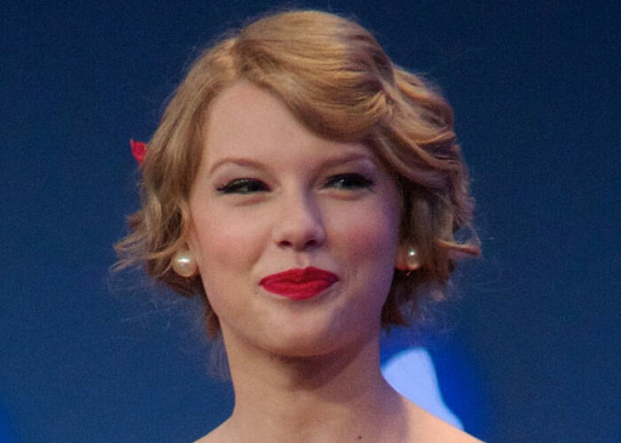 A celebrity, Taylor Swift, with a vintage hairstyle and red lipstick, smiles for a photo.
