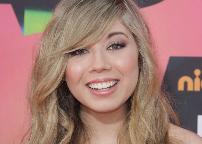 Jennette McCurdy, a smiling celebrity, poses for a photo on a red carpet.