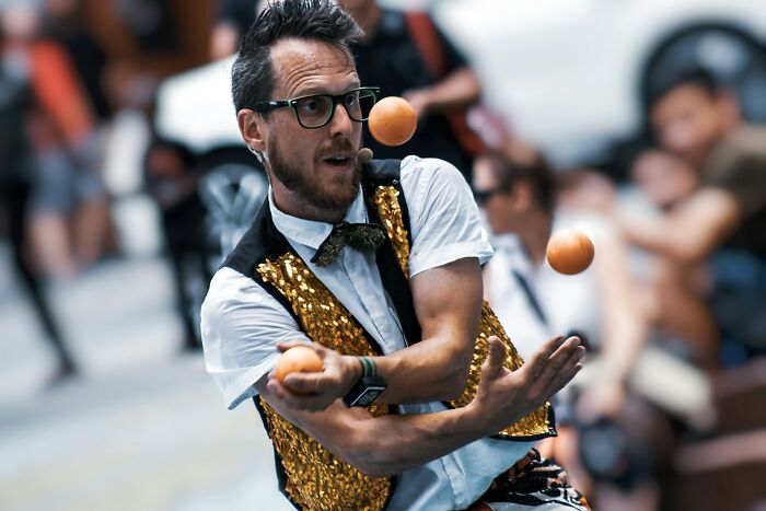 A man in a sparkly vest juggling oranges, illustrating strange jobs and unconventional ways to earn money.