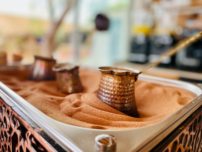 A close-up of three traditional Turkish coffee pots nestled in a bed of sand, showing a fascinating method of brewing.