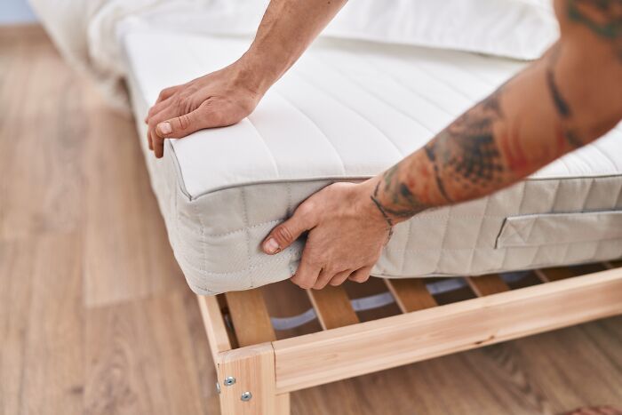 Hands adjusting a mattress on a bed frame, highlighting stories about guests.