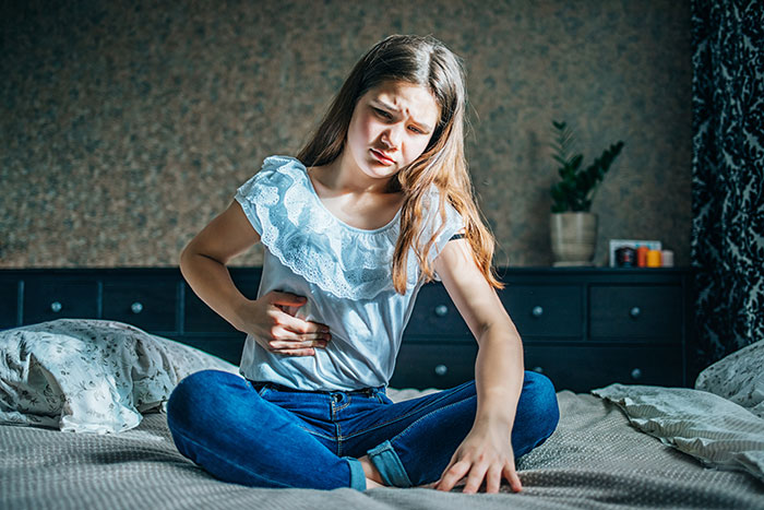 A teen holds her stomach, looking distressed, revealing her body was a lie from a controlling mom. A teen holds her stomach, looking distressed, revealing her body was a lie from a controlling mom.