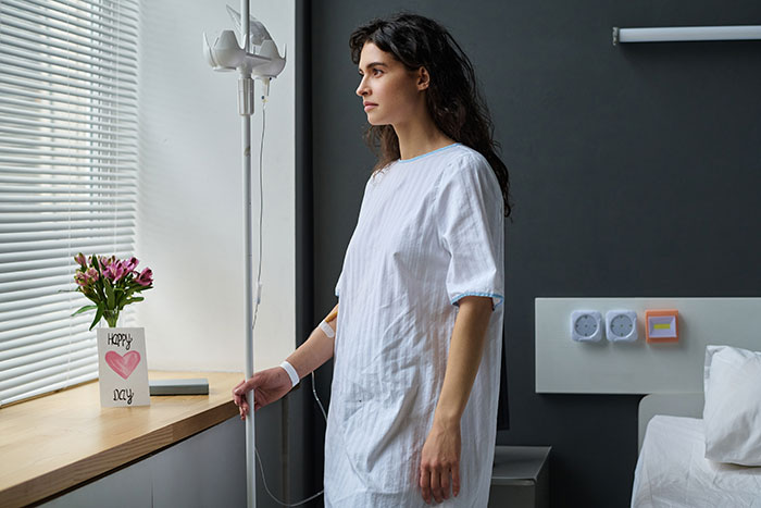 A young woman in a hospital gown, looking out a window. This represents a teen learning about her own body after escaping a controlling mom. A young woman in a hospital gown, looking out a window. This represents a teen learning about her own body after escaping a controlling mom.