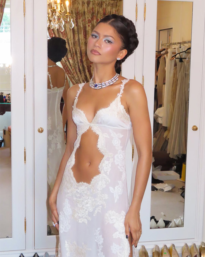 Zendaya modeling a white lace dress with cutouts and a statement necklace, reflecting her latest look in a mirror. Zendaya modeling a white lace dress with cutouts and a statement necklace, reflecting her latest look in a mirror.
