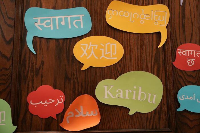 A wooden door adorned with colorful speech bubbles saying welcome in different languages, representing unsolved mysteries.
