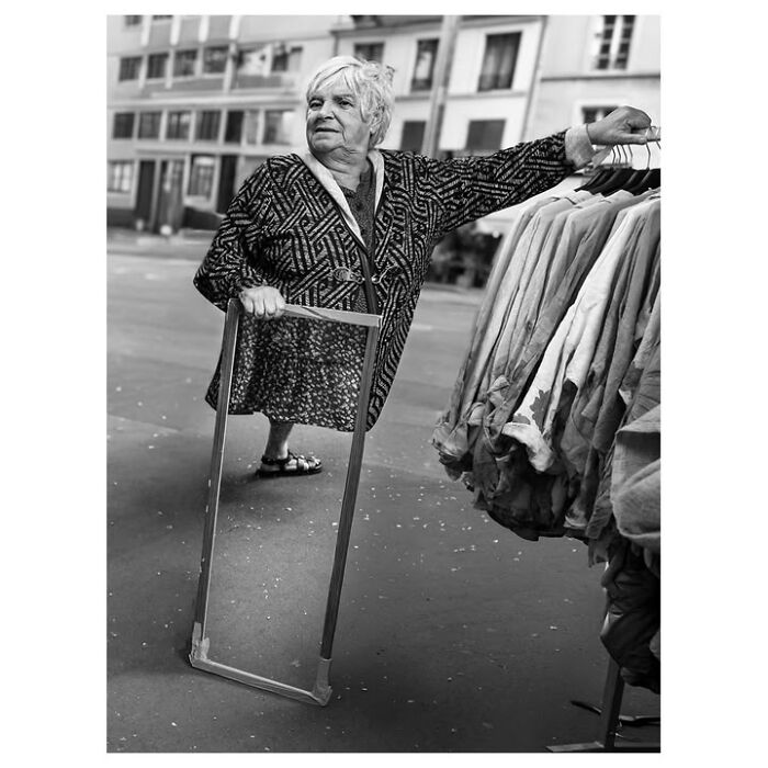 A perfectly timed street photo in Paris shows an elderly woman looking into a mirror on the street, a quirky Paris moment.