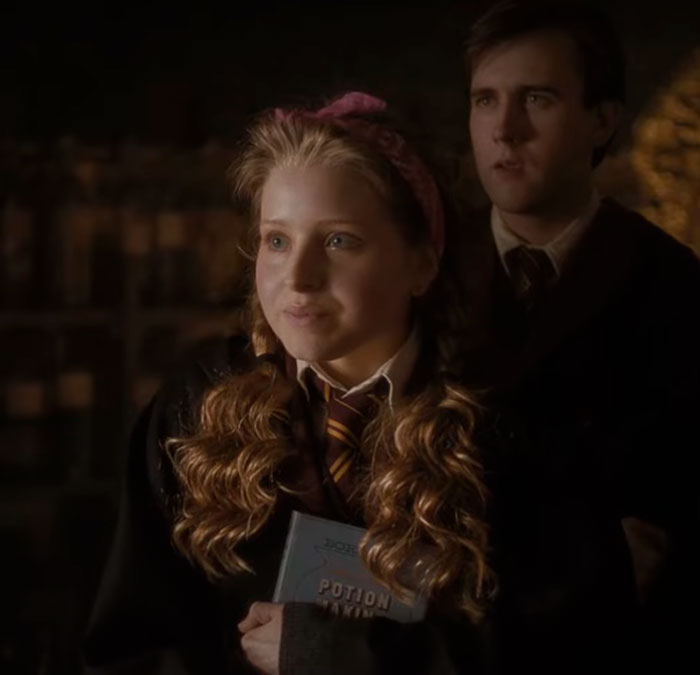 A young Harry Potter star, Jessie Cave, in character holding a Potions book while a male character stands behind her. A young Harry Potter star, Jessie Cave, in character holding a Potions book while a male character stands behind her.