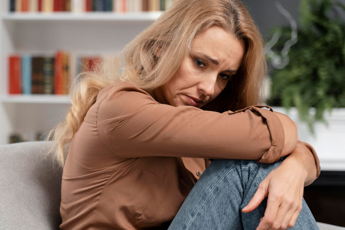 A sad woman looking down, with blonde hair, reflecting on her MIL driving her to leave her son. A sad woman looking down, with blonde hair, reflecting on her MIL driving her to leave her son.