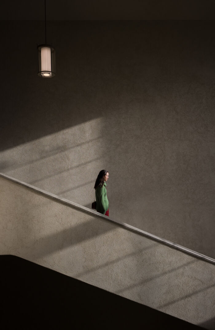 Moody minimalist photography featuring a woman walking up a staircase, illuminated by a single light source and shadows.