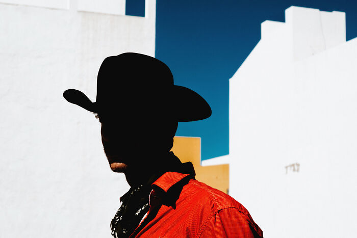 Extraordinary minimalist photography featuring a silhouetted man in a cowboy hat against white buildings and blue sky.