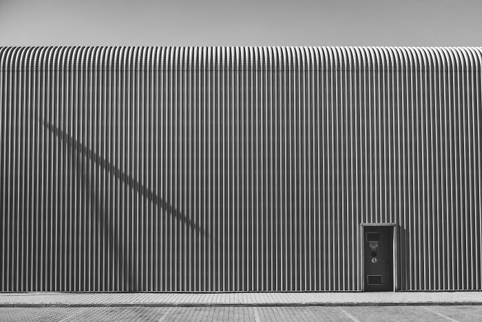 A minimalist photography award winner showing a textured wall with a small door and a prominent shadow, in black and white.