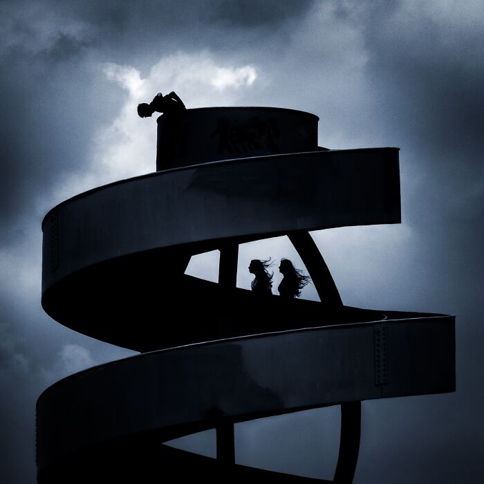 A silhouetted spiral structure with two figures and another on top, a captivating entry in the Minimalist Photography Awards.