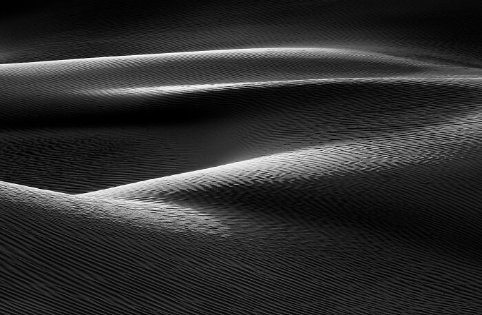 Dramatic black and white sand dunes with sharp shadows and highlights, an extraordinary example of minimalist photography.