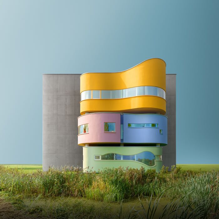 A vibrant, colorful, stacked, wavy building stands against a plain concrete wall, reflecting minimalist photography.