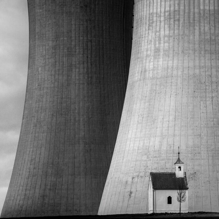 A minimalist photography award winner, capturing a tiny chapel dwarfed by two massive cooling towers of a power plant.