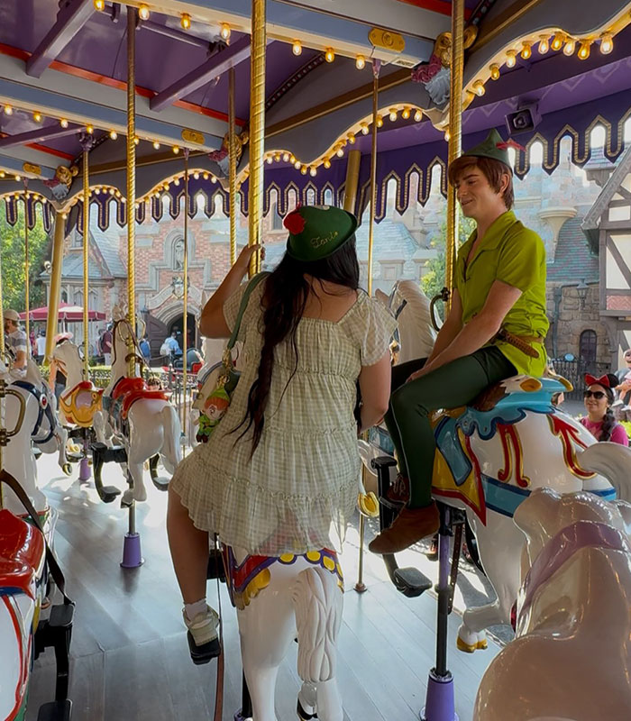The Peter Pan girl rides a carousel horse next to a Peter Pan character, fueling her Peter Pan obsession.