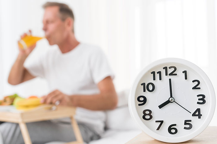 Man drinking juice with a clock showing 8 AM, representing a common breakfast habit linked to higher mortality risk. Man drinking juice with a clock showing 8 AM, representing a common breakfast habit linked to higher mortality risk.