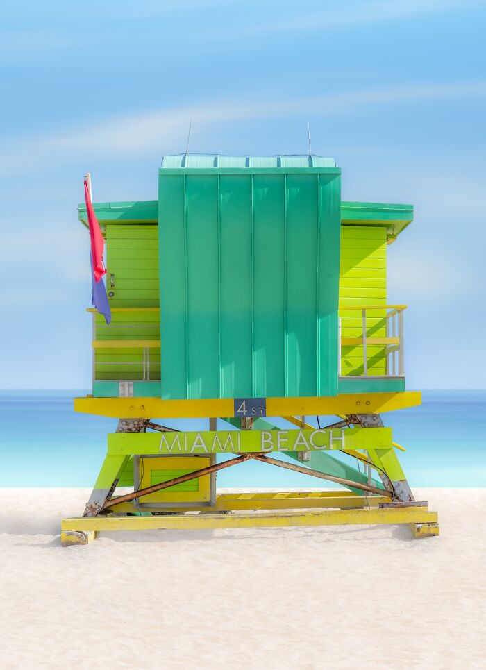 A vibrant pink and orange lifeguard stand on a white sand beach with a clear blue sky, demonstrating minimalist photography.