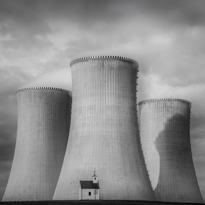 A minimalist photography award winner, capturing a tiny chapel dwarfed by two massive cooling towers of a power plant.