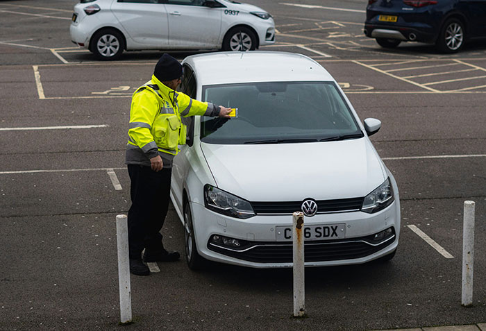 A parking attendant placing a penalty charge notice on a white car in the world's most beautiful village, targeting tourists. A parking attendant placing a penalty charge notice on a white car in the world's most beautiful village, targeting tourists.
