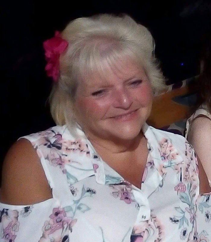 A blonde woman smiling with a pink flower in her hair, discussing the surgeon's horrific crimes.