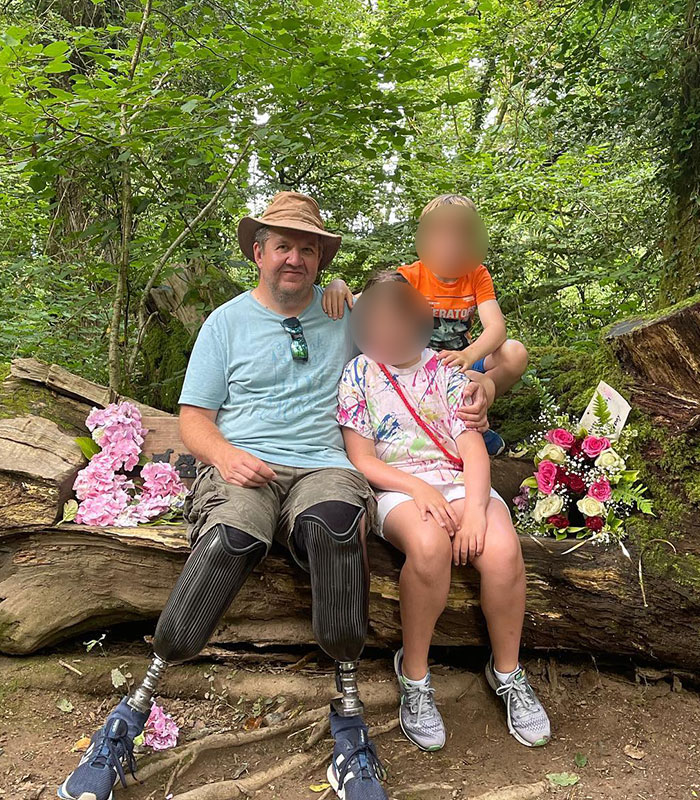 A man with amputated legs sitting on a log with two children, showing the impact of the surgeon's crimes.