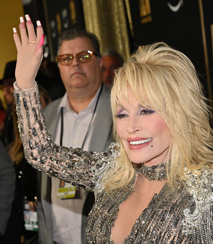 Dolly Parton waving, with her hands covered by sparkling skin-colored gloves. Dolly Parton waving, with her hands covered by sparkling skin-colored gloves.