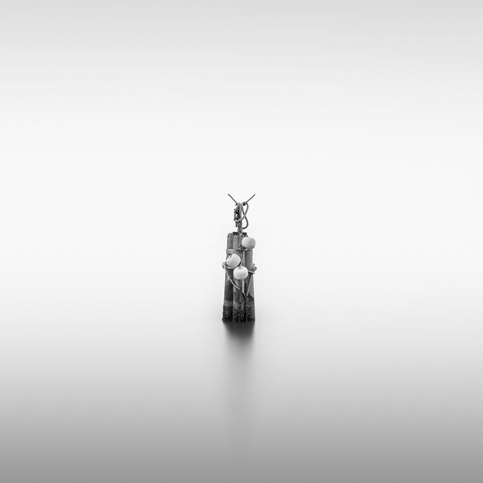 A minimalist photography close-up of a dark, narrow object with three white pearl-like beads, against a subtle gradient background.