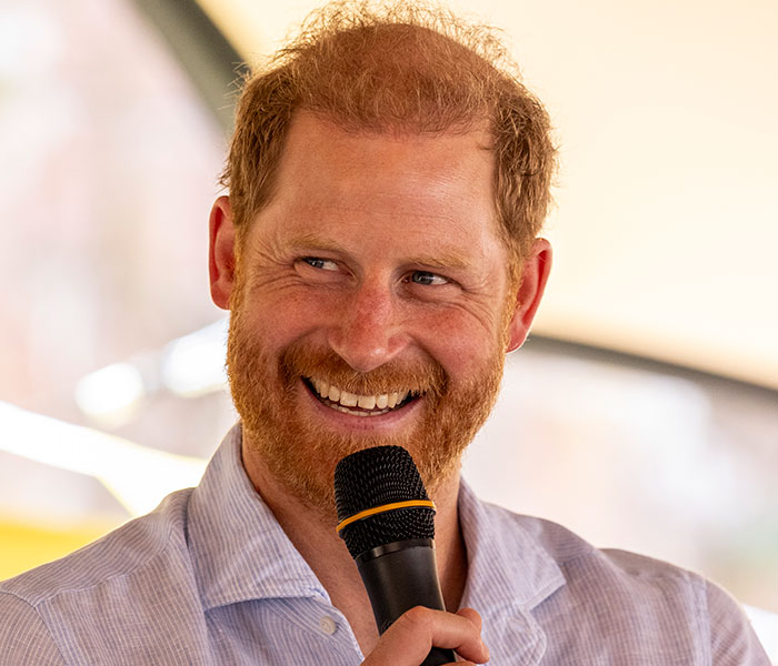 Prince Harry smiles, holding a microphone, hinting at his role in the family tension. Prince Harry smiles, holding a microphone, hinting at his role in the family tension.