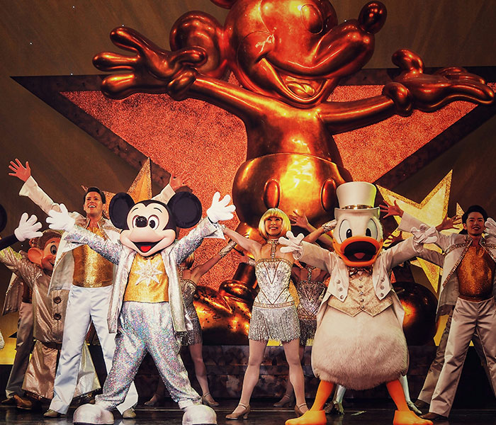 Disney Cast Member performs onstage during a Disney cruise show, featuring Mickey Mouse and Donald Duck characters.