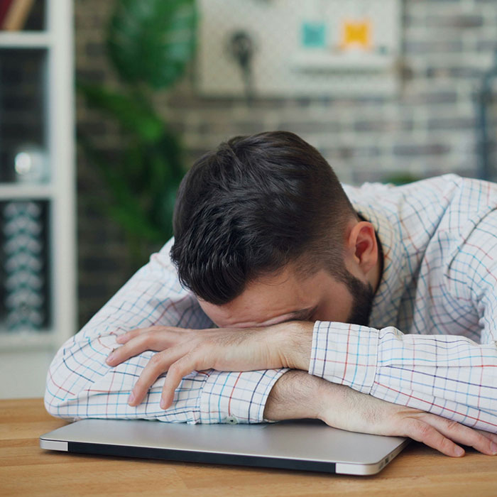 Man resting his head on a laptop, illustrating fatigue as a cancer symptom people dismiss. Man resting his head on a laptop, illustrating fatigue as a cancer symptom people dismiss.