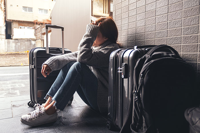 A woman sits on the ground with her luggage, looking distressed after a secret police call and deportation.