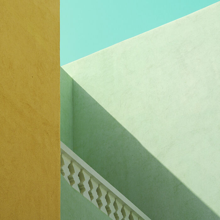 An abstract minimalist photography composition featuring a golden wall, light green wall, and turquoise sky, creating sharp angles.